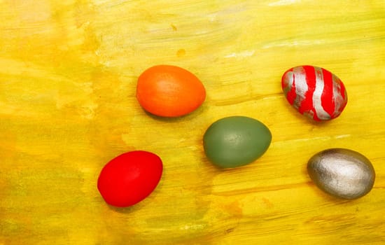 Red, orange, green, metallic eggs on an orange textured background. Five decorative handmade eggs on an orange canvas.