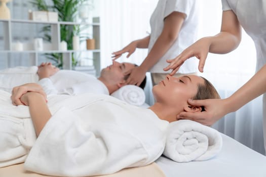 Caucasian couple enjoying relaxing anti-stress head massage and pampering facial beauty skin recreation leisure in dayspa modern light ambient at luxury resort or hotel spa salon. Quiescent