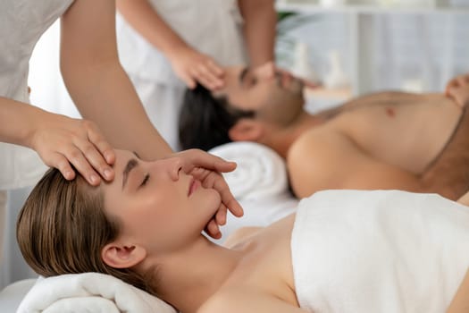 Caucasian couple enjoying relaxing anti-stress head massage and pampering facial beauty skin recreation leisure in dayspa modern light ambient at luxury resort or hotel spa salon. Quiescent