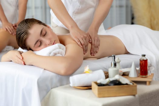 Caucasian couple customer enjoying relaxing anti-stress spa massage and pampering with beauty skin recreation leisure in day light ambient salon spa at luxury resort or hotel. Quiescent