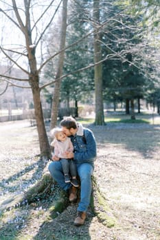 Dad kisses a little girl on his knees sitting on a stump in a flowering meadow. High quality photo