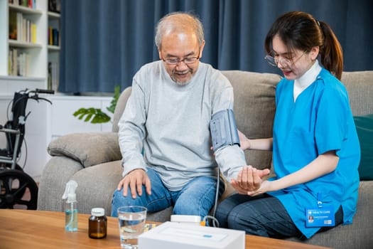 Asian doctor woman examine do checking old man client heart rate with pulsimeter monitor, nurse visit patient senior man at home she measuring arterial blood pressure on arm in living room, Healthcare