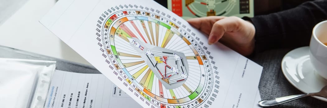 TVER, RUSSIA - FEBRUARY 12, 2023: A woman at the table is studying a rave mandala by human design. Rave mandala on the table close-up. The concept of esoteric teachings