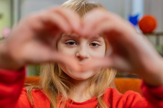 I love you. Caucasian child kid girl makes symbol of love, showing heart sign to camera, express romantic feelings, express sincere positive feelings. Charity, gratitude, donation. Female teen at home