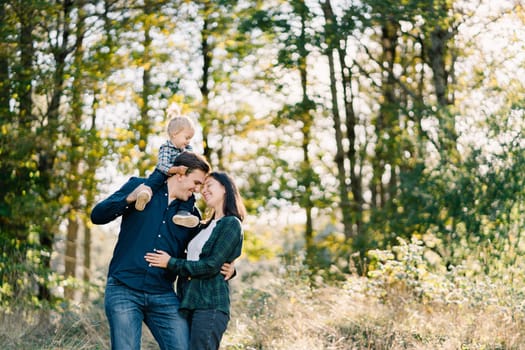 Dad with a little girl on his shoulders hugs mom touching her forehead. High quality photo