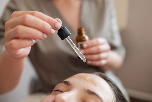 Doctor drops some medicine to the forehead of a girl client before using meso roller with microneedles