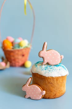 Still life with two pink gingerbread in the form of a rabbit on an Easter cake and a basket with colorful eggs behind