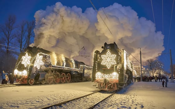 Russia, Peterhof, 07 January 2024: Two Santa Claus Trains leave the magically decorated building of the New Peterhof station, huge steam clubs, many people, incredible lighting. High quality photo