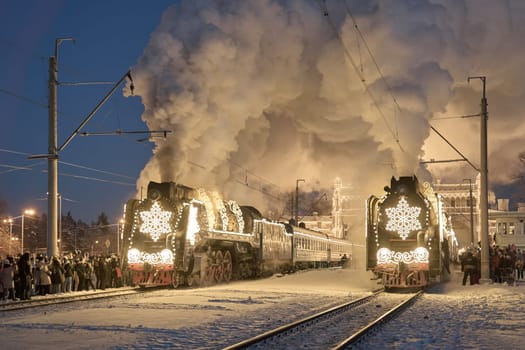 Russia, Peterhof, 07 January 2024: Two Santa Claus Trains leave the magically decorated building of the New Peterhof station, huge steam clubs, many people, incredible lighting. High quality photo