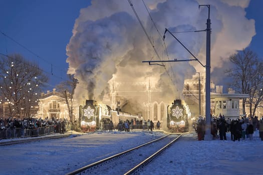 Russia, Peterhof, 07 January 2024: Two Santa Claus Trains leave the magically decorated building of the New Peterhof station, huge steam clubs, many people, incredible lighting. High quality photo