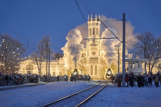 Russia, Peterhof, 07 January 2024: Two Santa Claus Trains leave the magically decorated building of the New Peterhof station, huge steam clubs, many people, incredible lighting. High quality photo