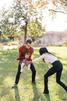 Mom tickles a little laughing girl in her dad arms in the garden. High quality photo