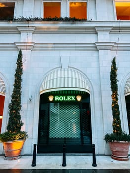 Trees in tubs decorated with luminous garlands near the store window. Caption: Rolex. High quality photo