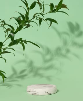 Empty round white marble stand on a green background and green leaves, a place to display cosmetics and products