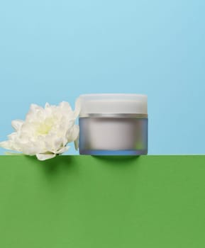 Glass jar with cosmetic cream, plastic lid. Blue background 