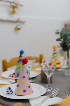 Beautiful view of a served table with white plates, conical colored birthday caps, glasses and forks with napkins on a wooden table, close-up side view.