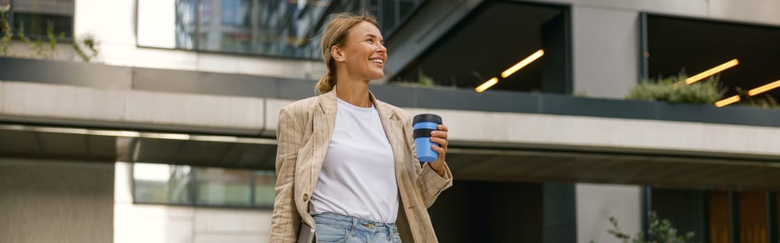 Stylish business woman drinking coffee during break time near office building and looks away