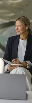 Pretty businesswoman making notes in note pad sitting on modern office background