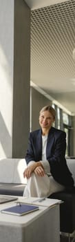 Pretty female entrepreneur working on laptop sitting in modern office hall and looks camera