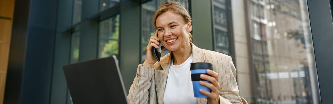 Smiling businesswoman talking on phone with client while working on laptop in office