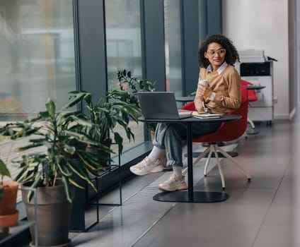 Smiling female freelancer have coffee break during working on laptop in modern coworking