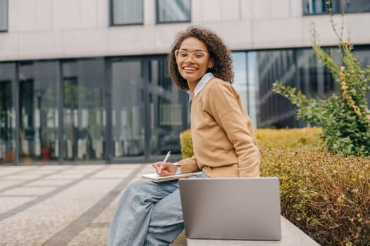 Female freelancer working laptop while sitting outside on background of office building