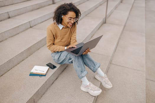 Smiling woman manager working laptop sitting on stairs on modern building background