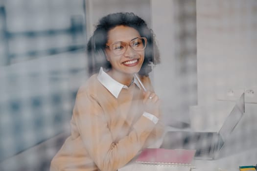 Pretty female freelancer working on laptop while sitting on modern coworking background