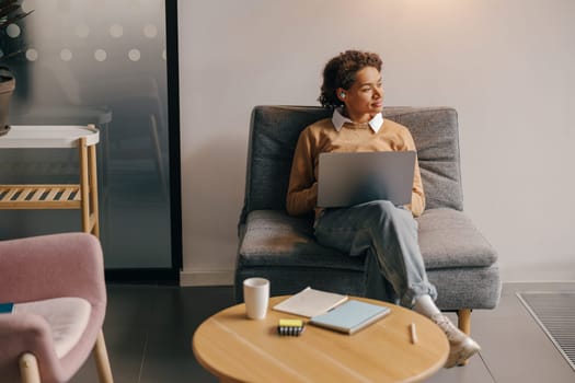 Smiling business woman using laptop while sitting on modern office background