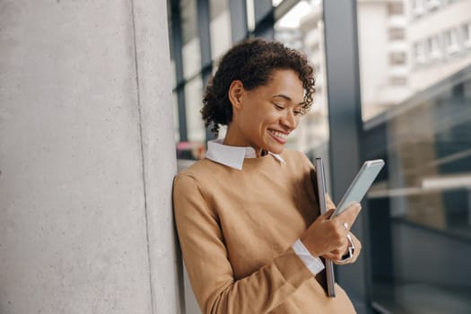 Smiling woman executive manager is using mobile phone standing in office during break time