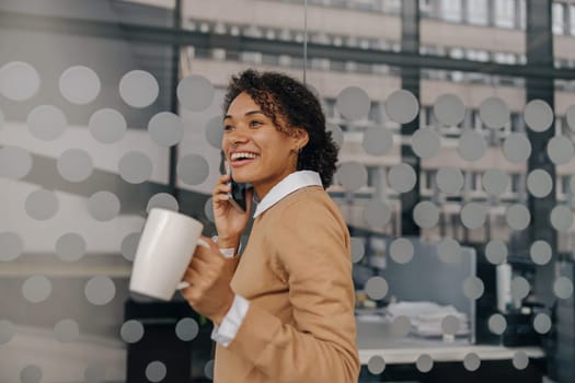 Smiling female freelancer is talking phone with client while standing on coworking background