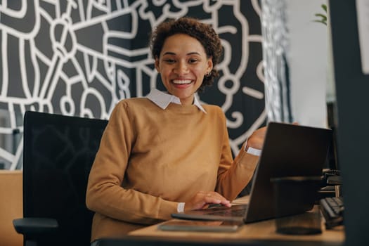 Pretty female freelancer working on laptop while sitting on modern coworking background