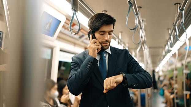 Professional caucasian project manager looking at watch while standing in train with blurred background. Professional business man calling to manager about investor surrounded by people. Exultant.