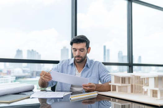 Skilled caucasian architect engineer holding blueprint on desk in modern office. Smart interior designer compared between blueprint and house model. Project, blueprint, construction, project. Tracery.