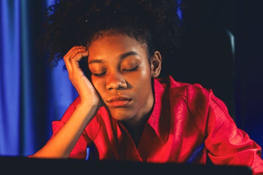 Exhausted and sleepy young African businesswoman taking a nap in her arm on desk at home office. Concept of thinking a lot projects until sleeping among unfinished online work. Tastemaker.