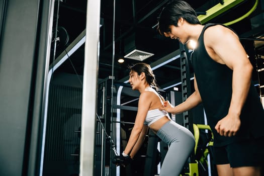 Personal trainer man teaching and support a young woman how to use a pull-down weight machine at the gym, with a smile on her face. GYM healthy lifestyle concept