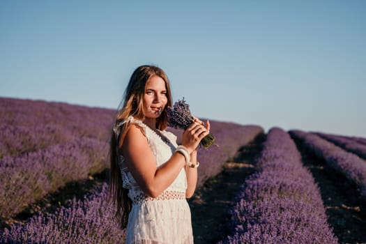 Close up portrait of young beautiful woman in a white dress and a hat is walking in the lavender field and smelling lavender bouquet.