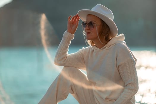 Happy blonde woman in a white suit and hat posing at the camera against the backdrop of the sea.