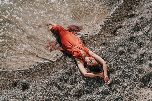 Woman red dress sea. Female dancer in a long red dress posing on a beach with rocks on sunny day.