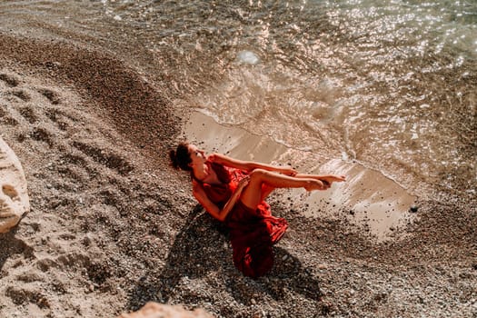 Woman red dress sea. Female dancer in a long red dress posing on a beach with rocks on sunny day.