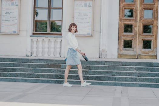 Woman staircase city. A business woman in a white shirt and denim skirt walks down the steps of an ancient building in the city.