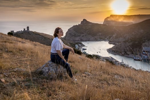 Happy woman on sunset in mountains. Woman siting with her back on the sunset in nature in summer. Silhouette