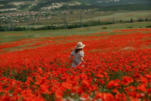 Field poppies woman. Happy woman in a white dress and hat stand with her back a blooming field of poppy. Field of blooming poppies