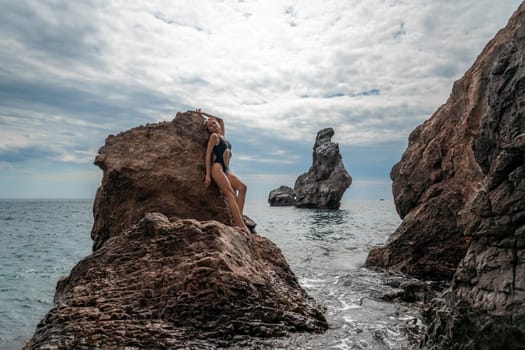 Woman swimsuit sea. Attractive blonde woman in a black swimsuit enjoying the sea air on the seashore around the rocks. Travel and vacation concept