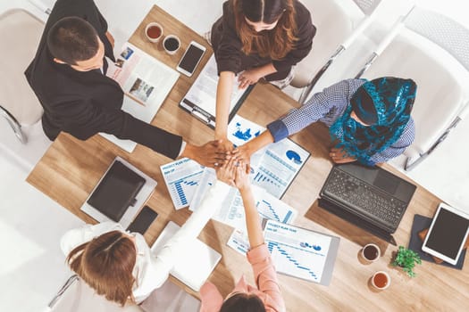 Businessmen and businesswomen joining hands in group meeting at multicultural office room showing teamwork, support and unity in business. Diversity workplace and corporate people working concept. uds