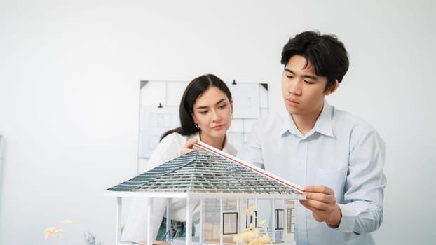 Professional young beautiful architect engineer using ruler and pencil measuring model roof length at modern office with blueprint hanged behind. Creative design and teamwork concept. Immaculate.