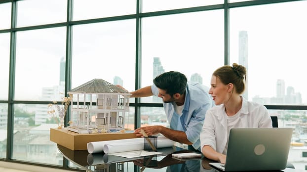 Smart architect engineer inspect house model while colleague using laptop analysis data. Professional designer team working together to design house model construction at modern office. Tracery