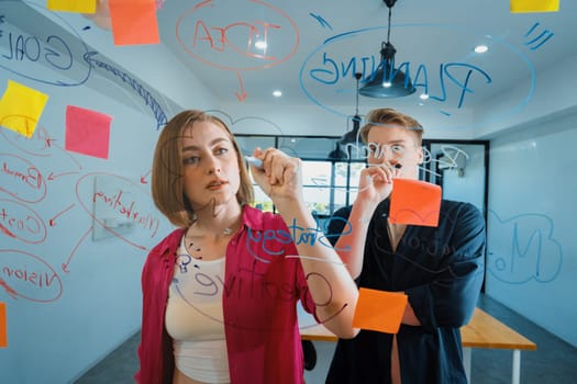 Couple of young creative start up business people brainstorming idea and solving problems by using sticky note and mind map at glass board, meeting room. discussing, working together. Immaculate.