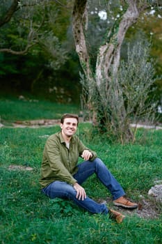 Young man sitting on green grass near the tree. High quality photo