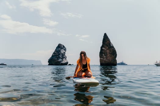 Close up shot of beautiful young caucasian woman with black hair and freckles looking at camera and smiling. Cute woman portrait in a pink bikini posing on a volcanic rock high above the sea